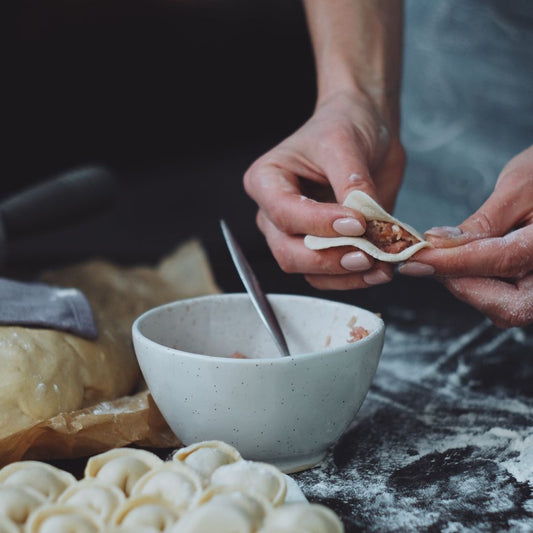 A pair of hands folding Chinese dumplings on a kitchen tabletop covered in flour.